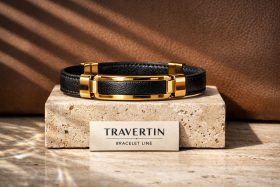 Bransoletka z czarnej skóry z elementami złotymi na kamiennym podłożu