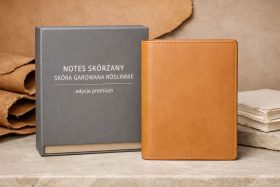 Skórzany notes w jasnobrązowej oprawie obok szarego pudełka z napisem