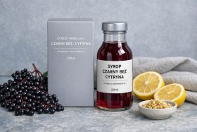 Butelka syropu czarny bez z cytryną i opakowanie z owocami i plasterkami cytryny