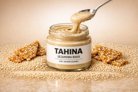 Słoik białej tahiny z łyżką i sezamowymi przekąskami na tle ziaren sezamu