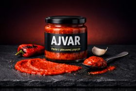 Słoik pasty ajvar z pieczonej papryki z łyżką i papryką na kamiennej powierzchni